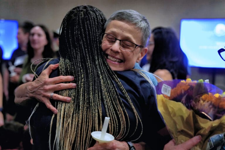 A woman embraces another woman warmly during a conference, showcasing a moment of support and camaraderie.